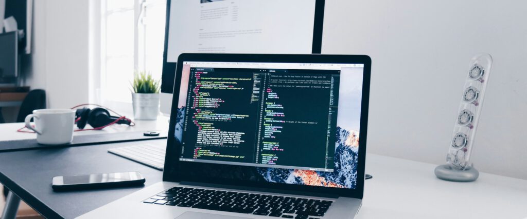 Heller Arbeitsplatz mit Laptop und Monitor, Code auf dem Bildschirm